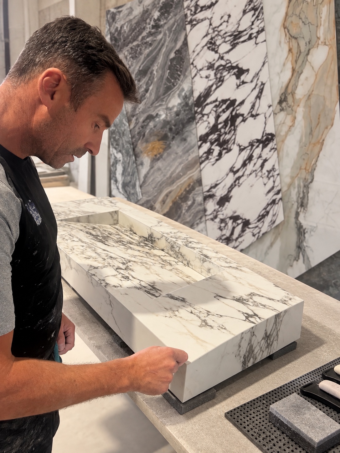 Craftsperson inspecting a bespoke marble basin beside natural stone slabs