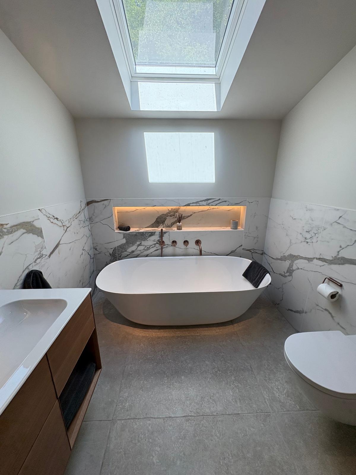Close-up of a marble bath surround niche with brushed bronze bath fillers