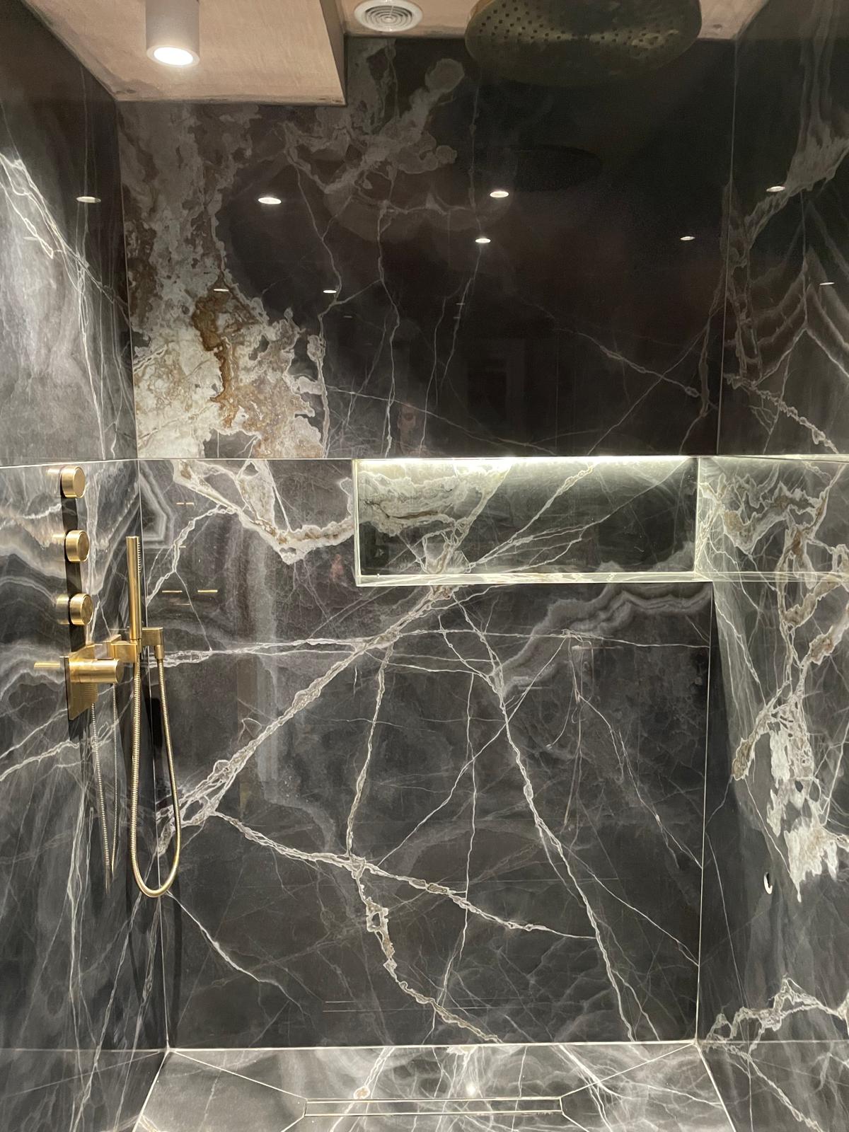 Book-matched dark marble shower with brass fittings and illuminated niche